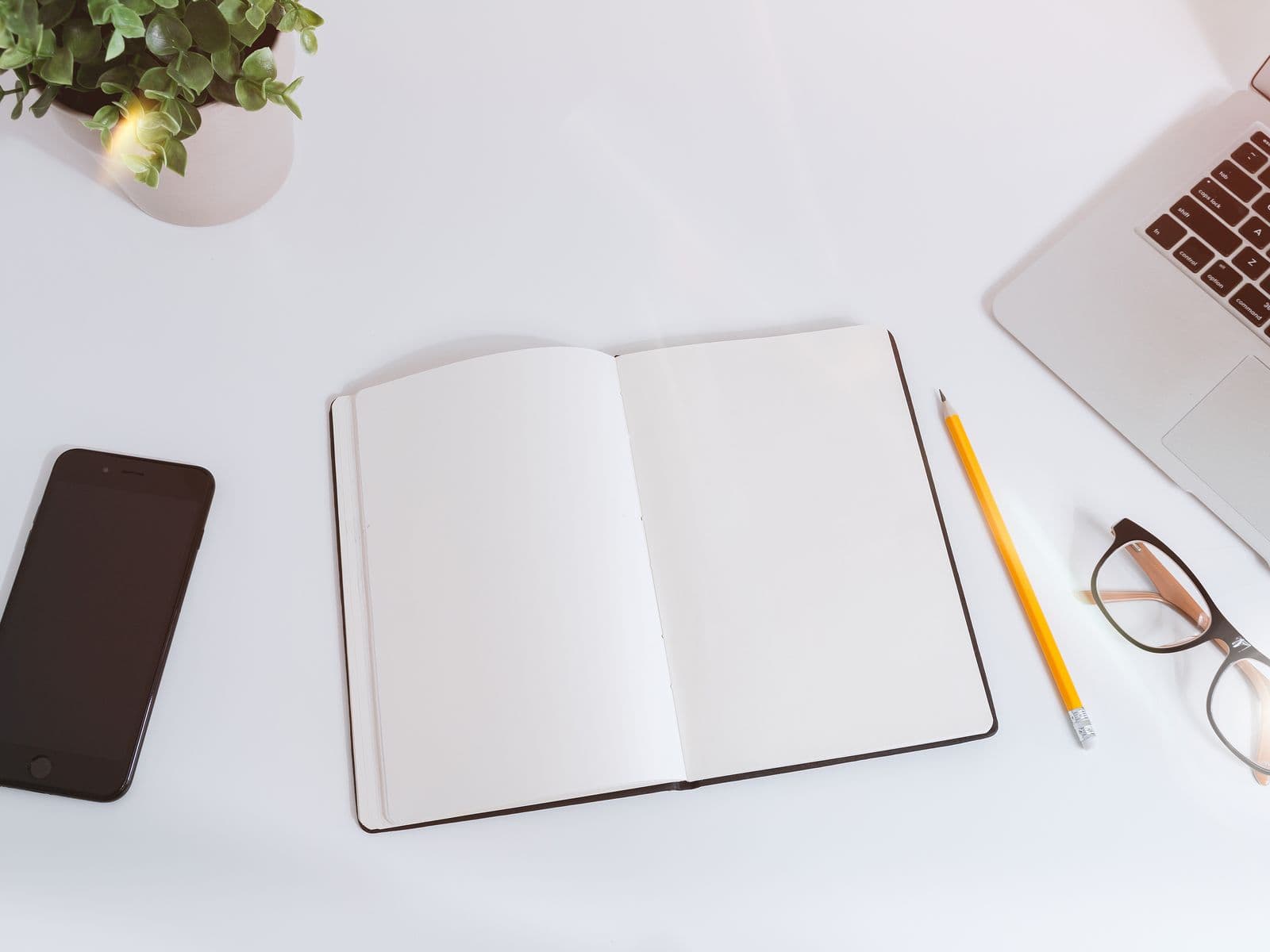 Desk with an open notebook, laptop, phone and glasses